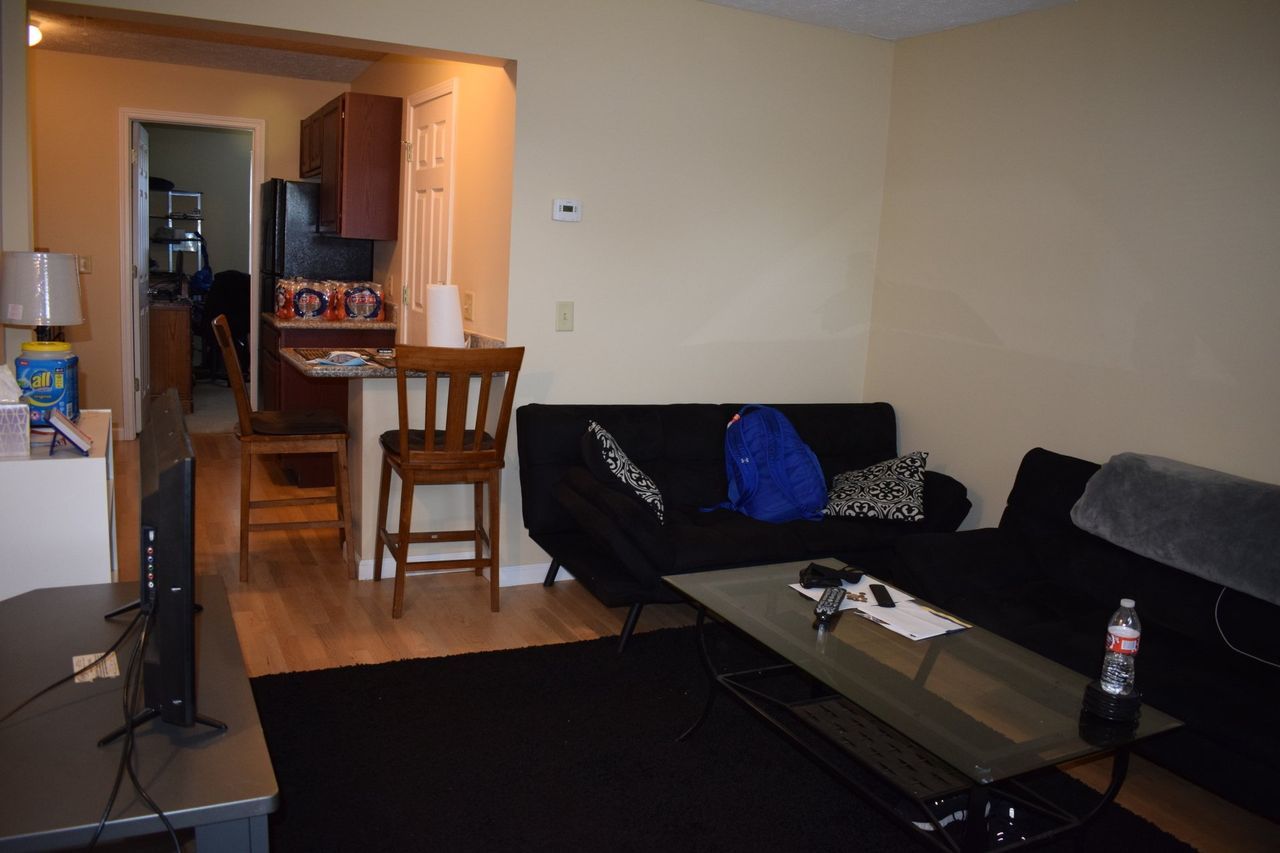 A living room with a black couch and a glass coffee table.