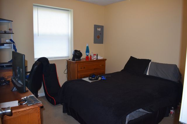 A bedroom with a bed, dresser, desk, and television.