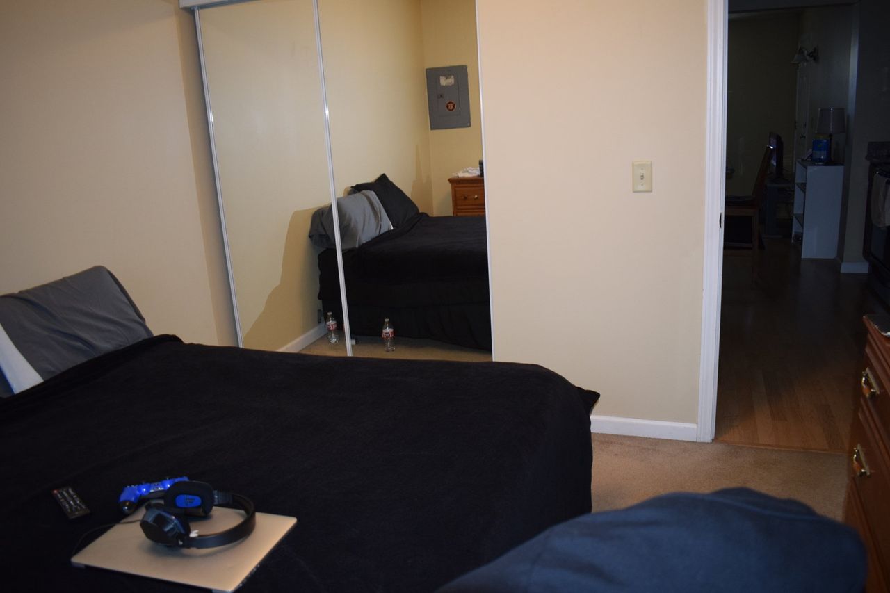 A bedroom with a bed, couch, headphones, and a mirror.