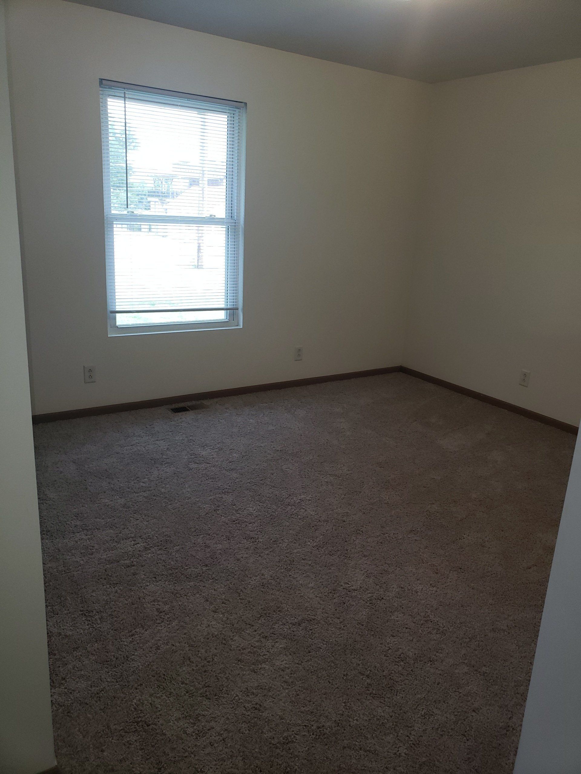 An empty bedroom with a window and a carpeted floor.