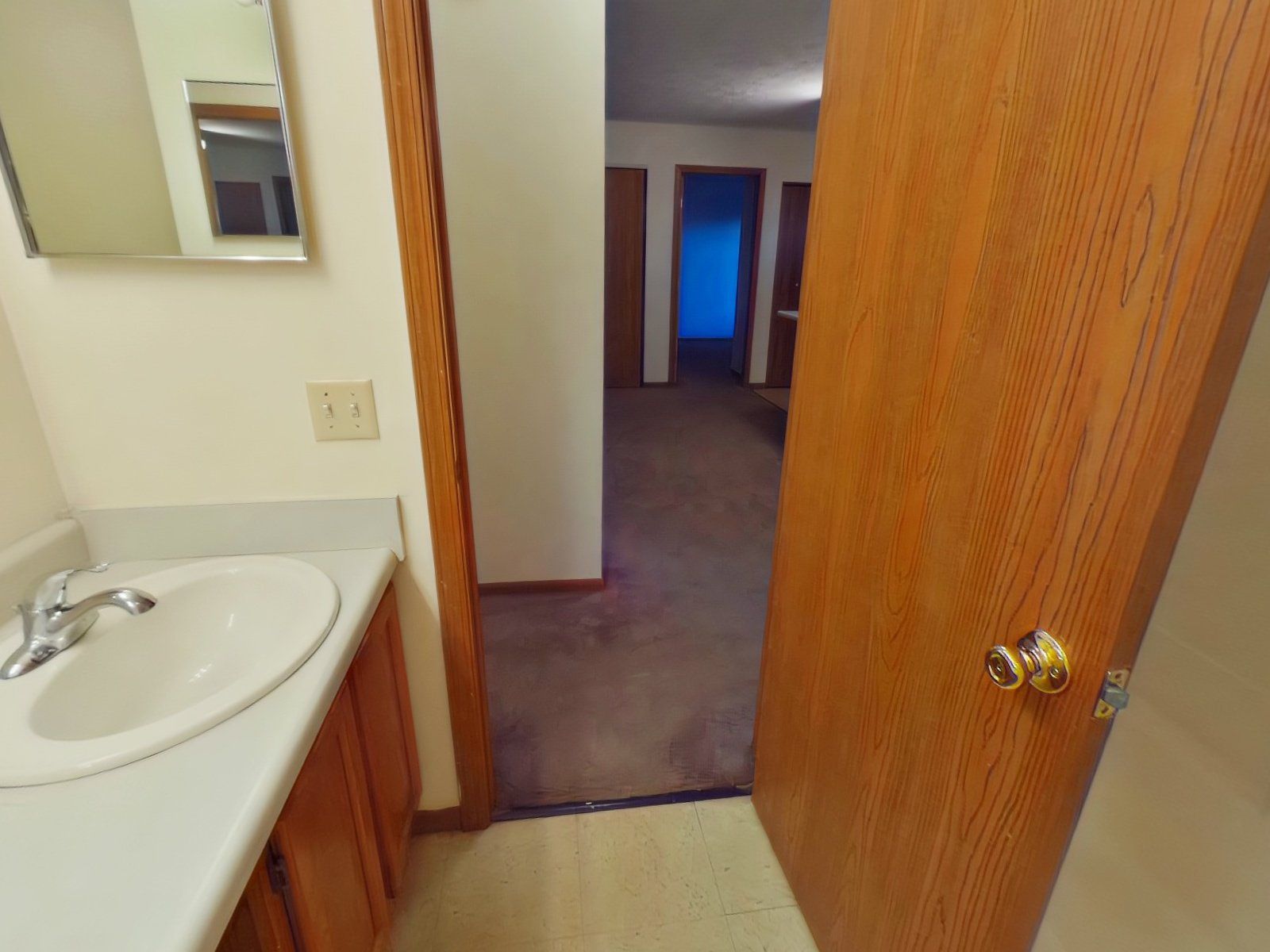 A bathroom with a sink, mirror, and door leading to a hallway.