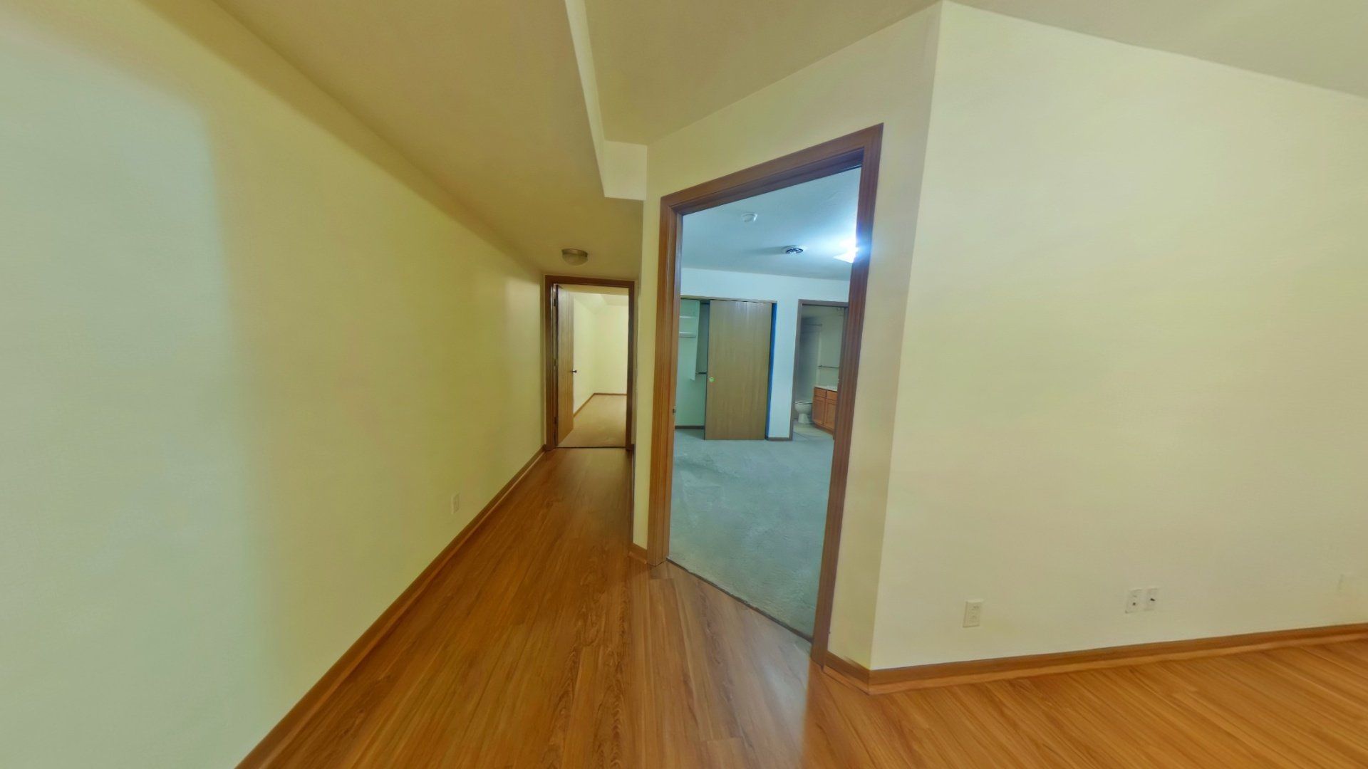 A long hallway with hardwood floors and a door leading to a room.