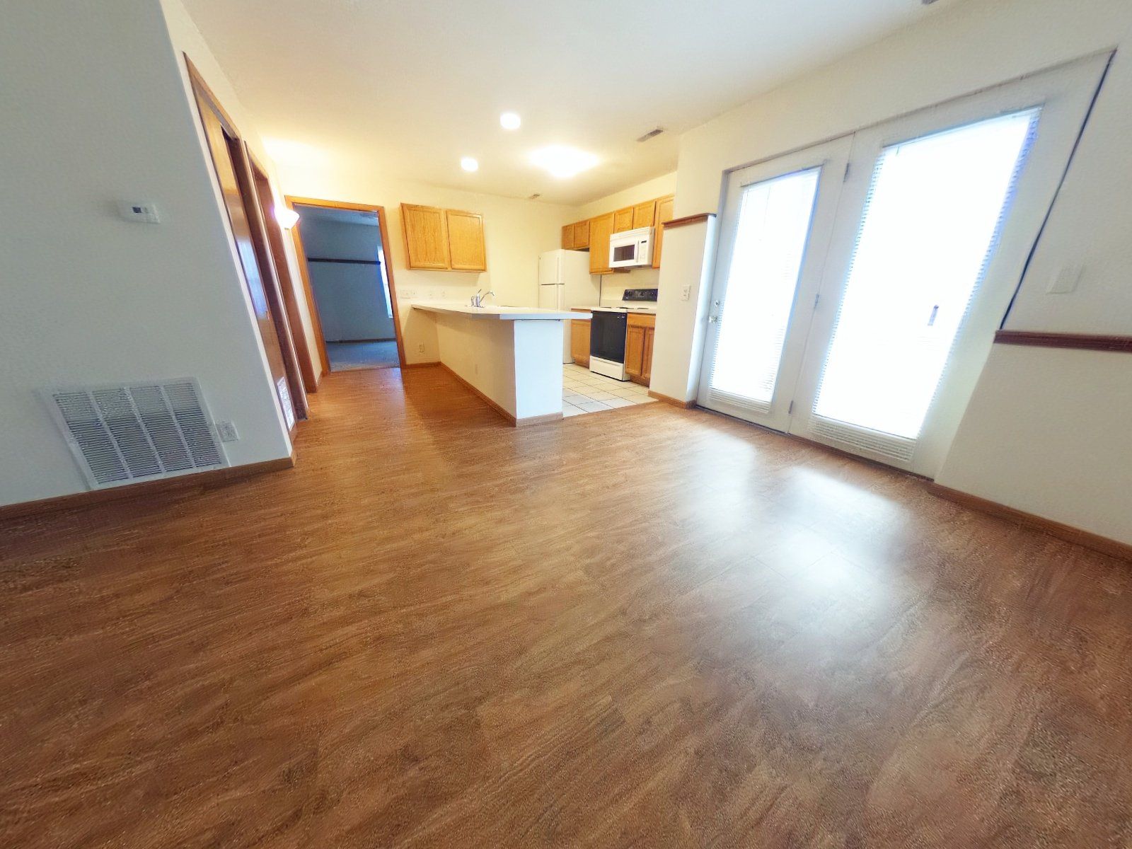 A living room with hardwood floors and a kitchen in the background.