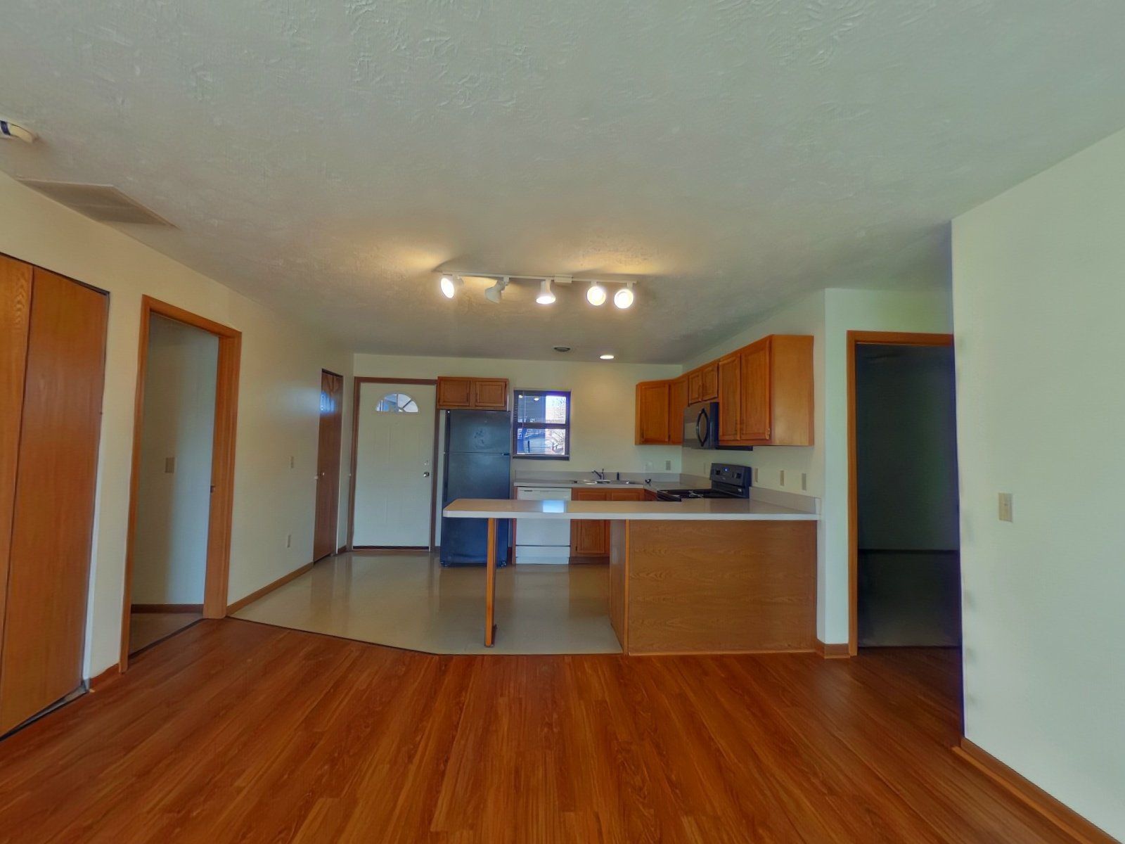 An empty kitchen with wooden floors and white cabinets.