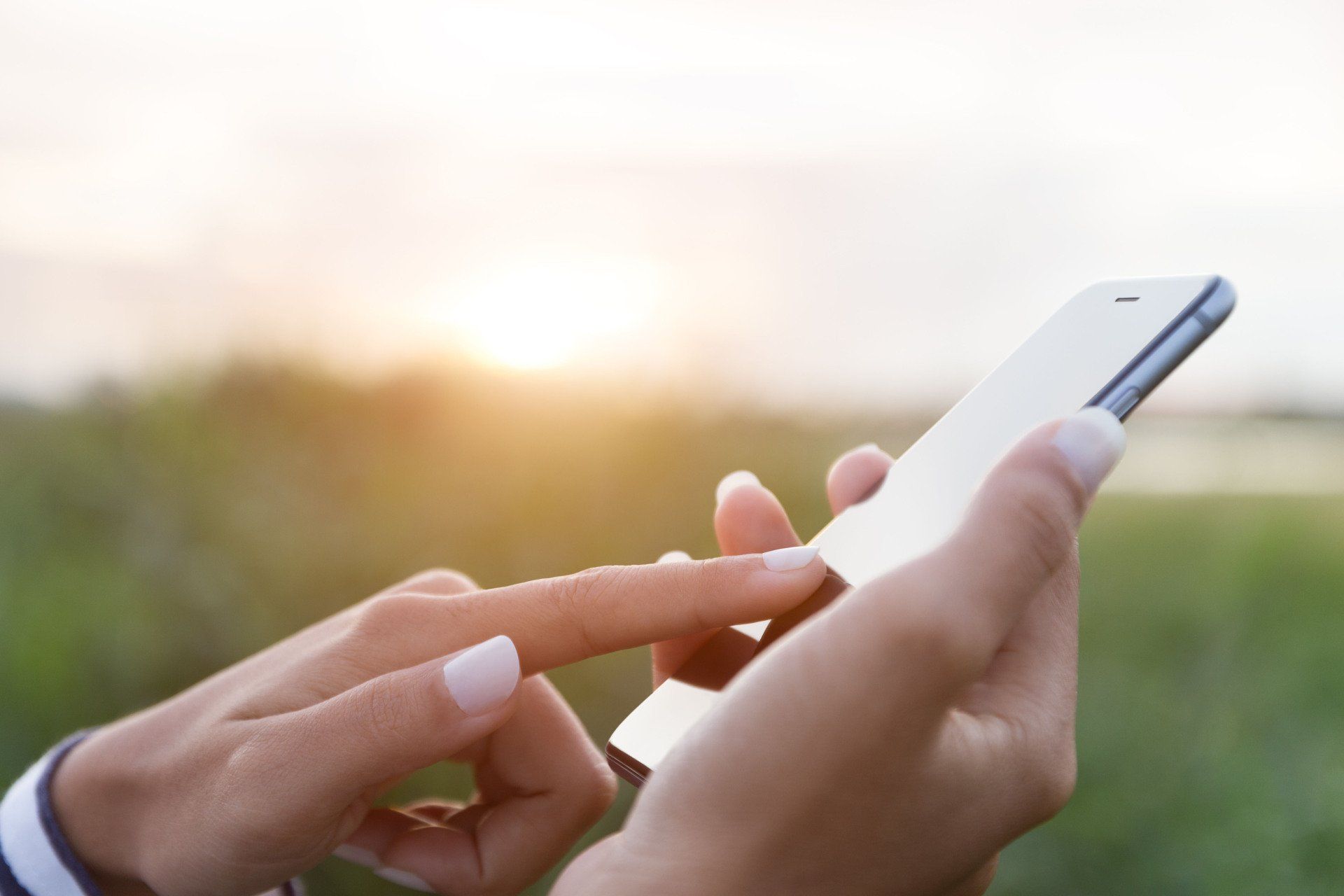A woman is using a cell phone in a field.