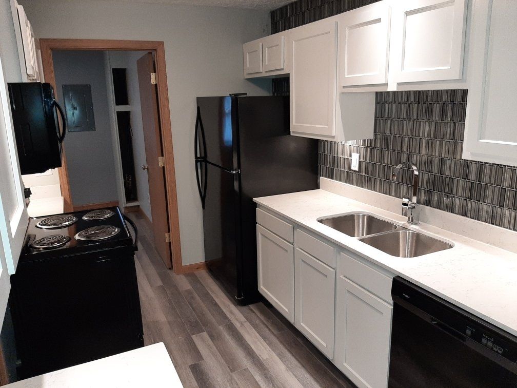 A kitchen with white cabinets, a black refrigerator, a black stove, a sink, and a dishwasher.