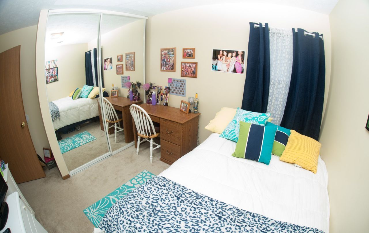 A bedroom with a bed, desk, chairs, and a large mirror.