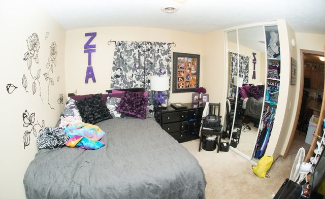 A bedroom with a bed and a purple letter ZTA on the wall.
