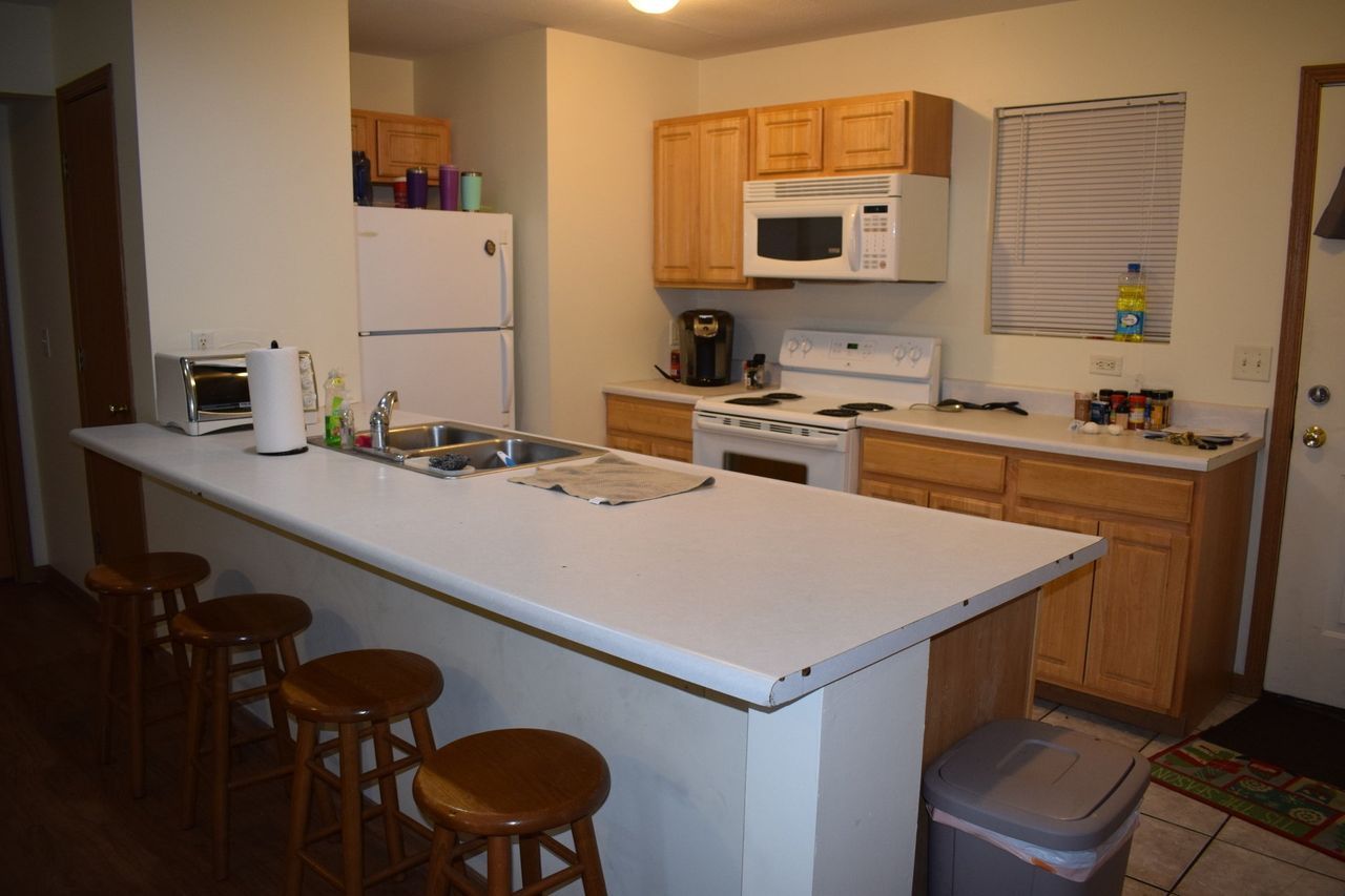 A kitchen with a stove, refrigerator, microwave, sink, and stools.