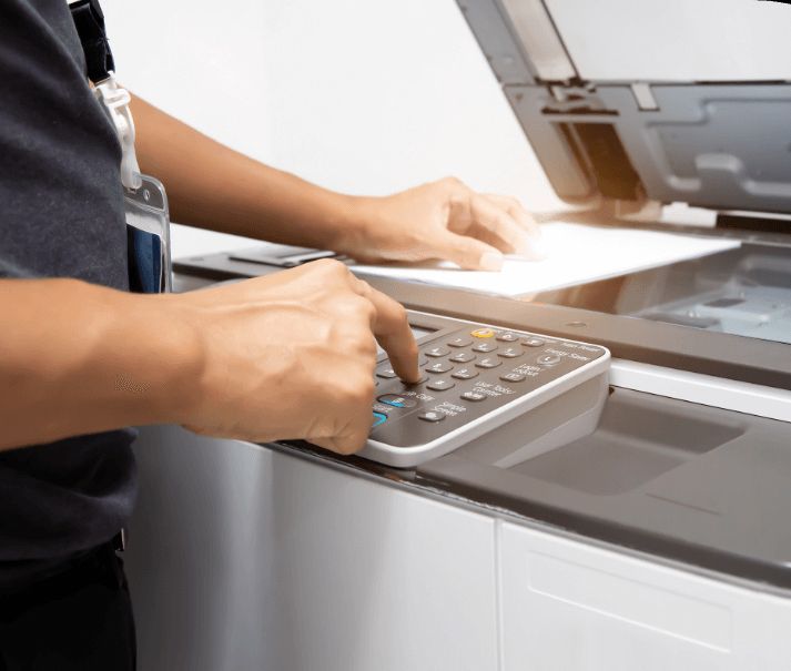 Person operating a copier, pressing buttons, with a paper placed inside.