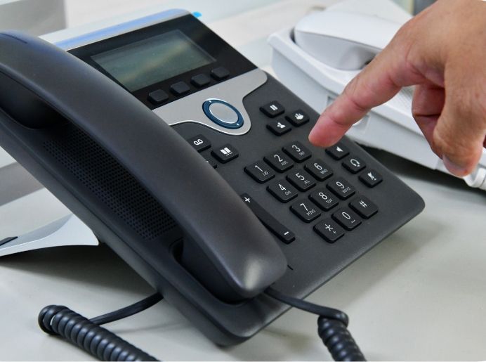 Person's finger pressing a button on a black office phone.