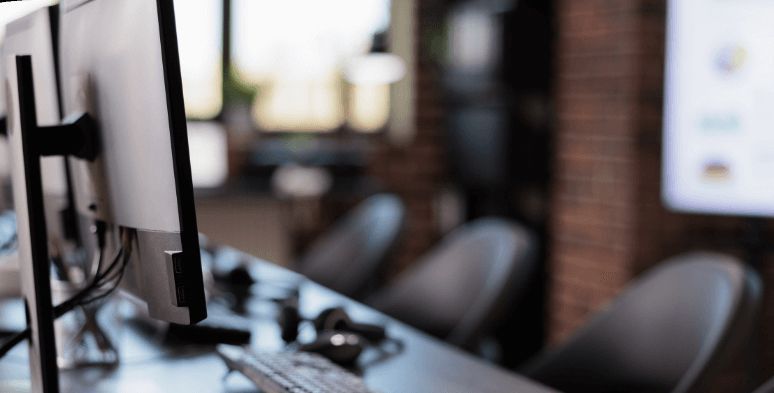 Computer monitors and chairs in an office space with a brick wall and blurred background.