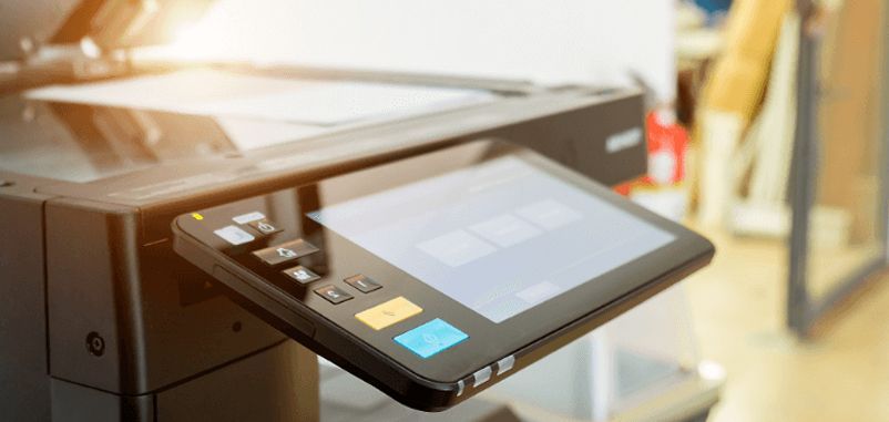 Close-up of a black office copier with a touch screen control panel. Sunlight is visible.