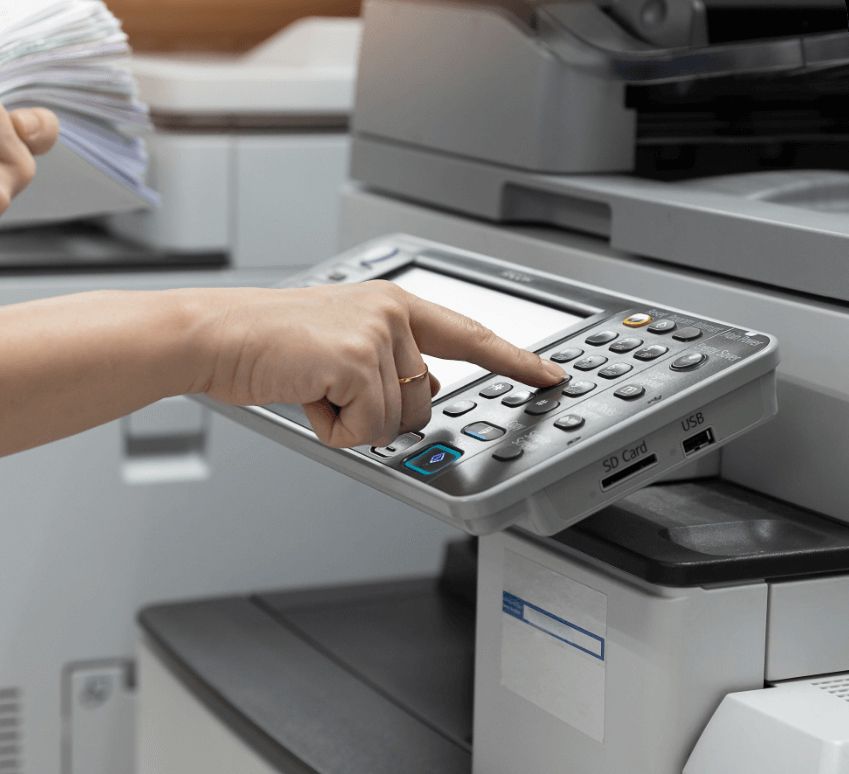 Person's hand presses buttons on a printer control panel while holding a stack of papers.