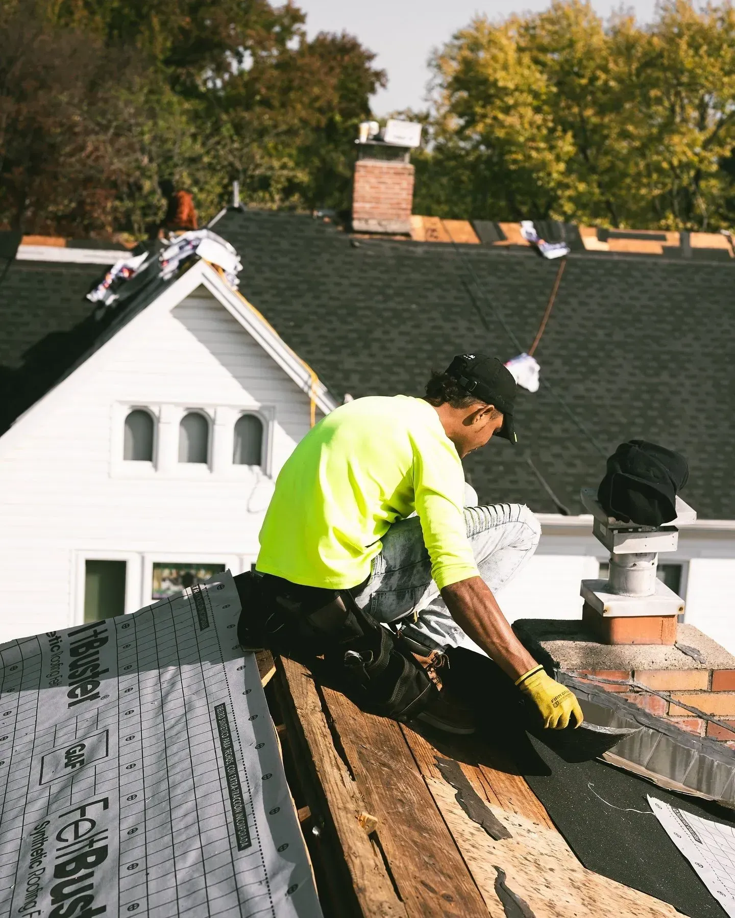 A man in a neon yellow shirt is working on a roof.
