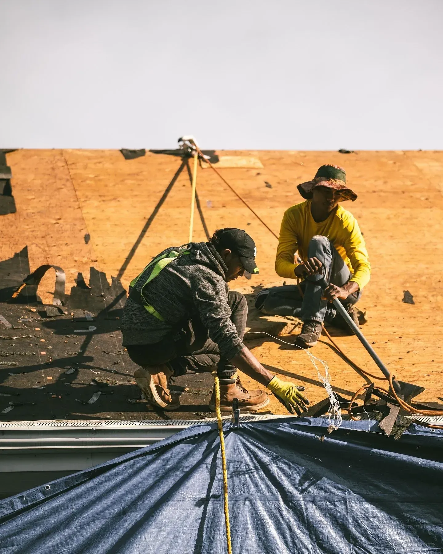 Two men are working on a roof with a tarp.