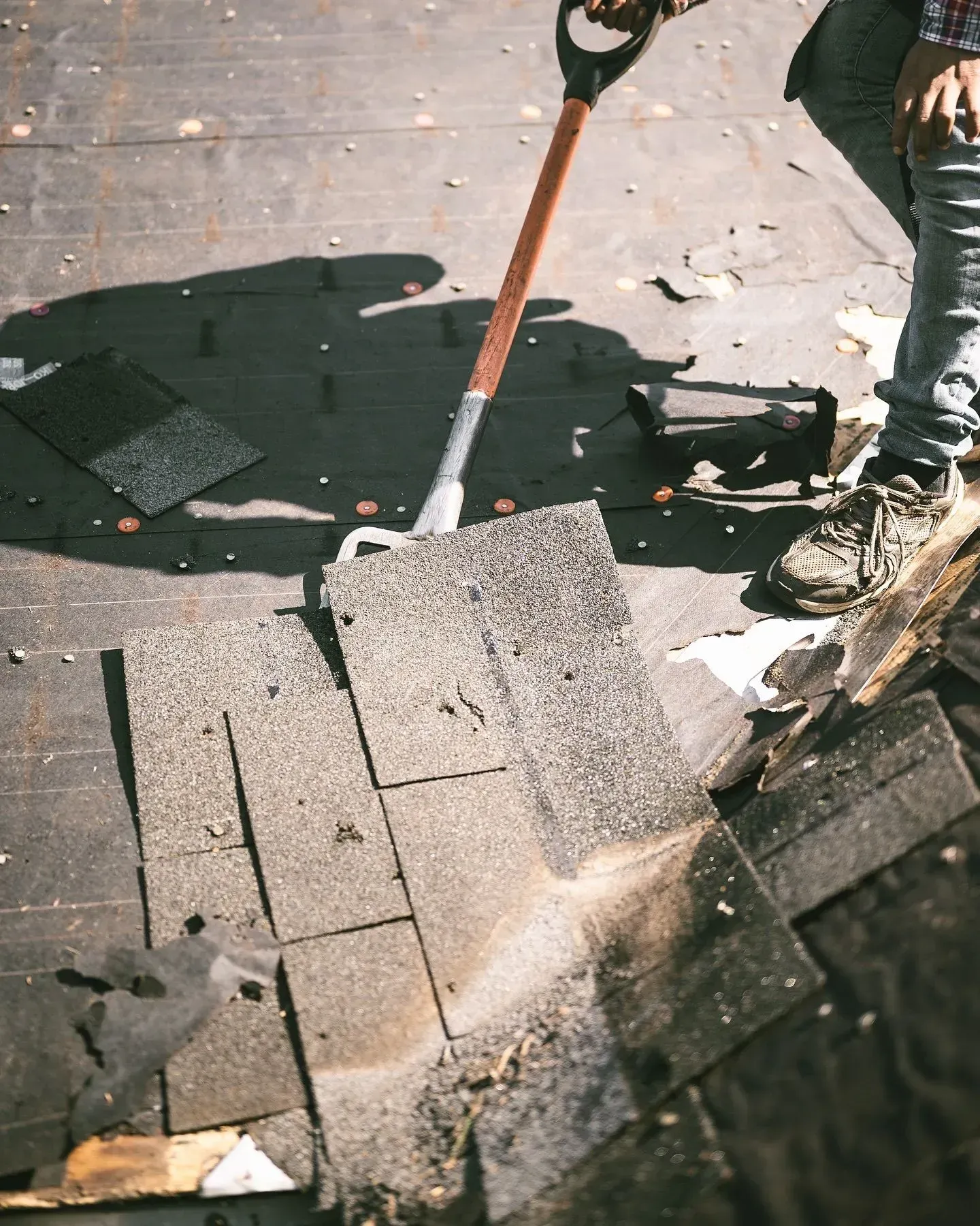 A person is using a shovel to remove shingles from a roof.