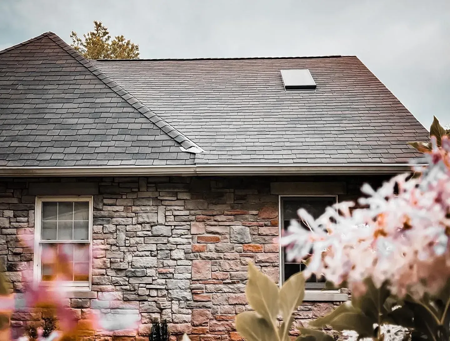 A brick house with a slate roof and flowers in front of it.