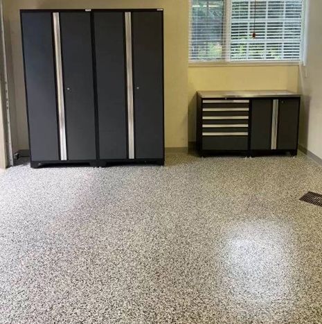 A garage with a concrete floor, cabinets, drawers and a window.