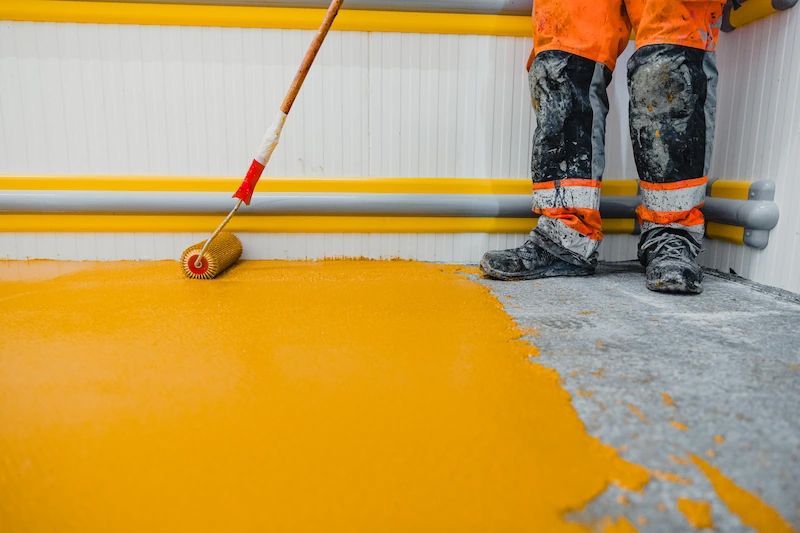 A man is painting a concrete floor with a roller.