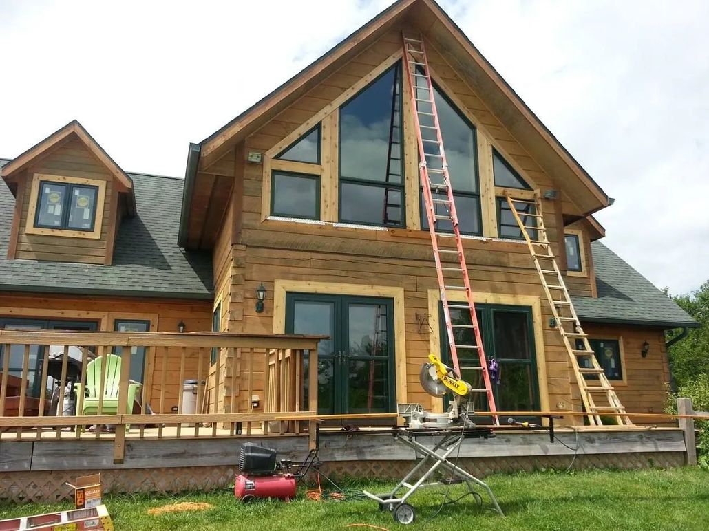 Log cabin under construction; ladders against the house, saw and compressor on the lawn.