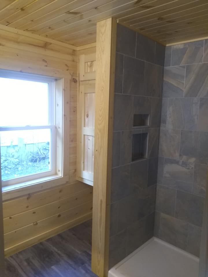 Bathroom interior with gray tiled shower and wooden accents, next to a window.