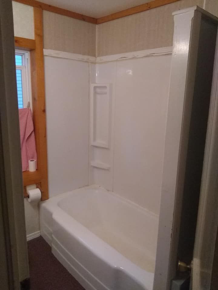 Small white bathtub with a built-in shower surround. Open doorway on the right. Pink towel visible on the left.