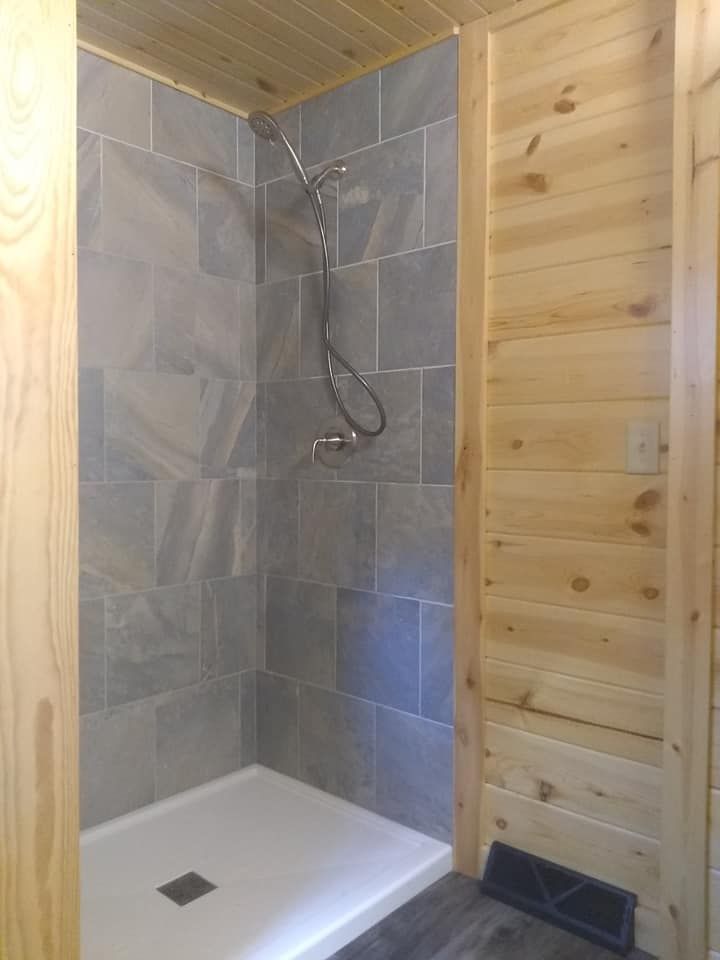 Shower with gray tiled walls, white base, wood paneling, and a metal showerhead.