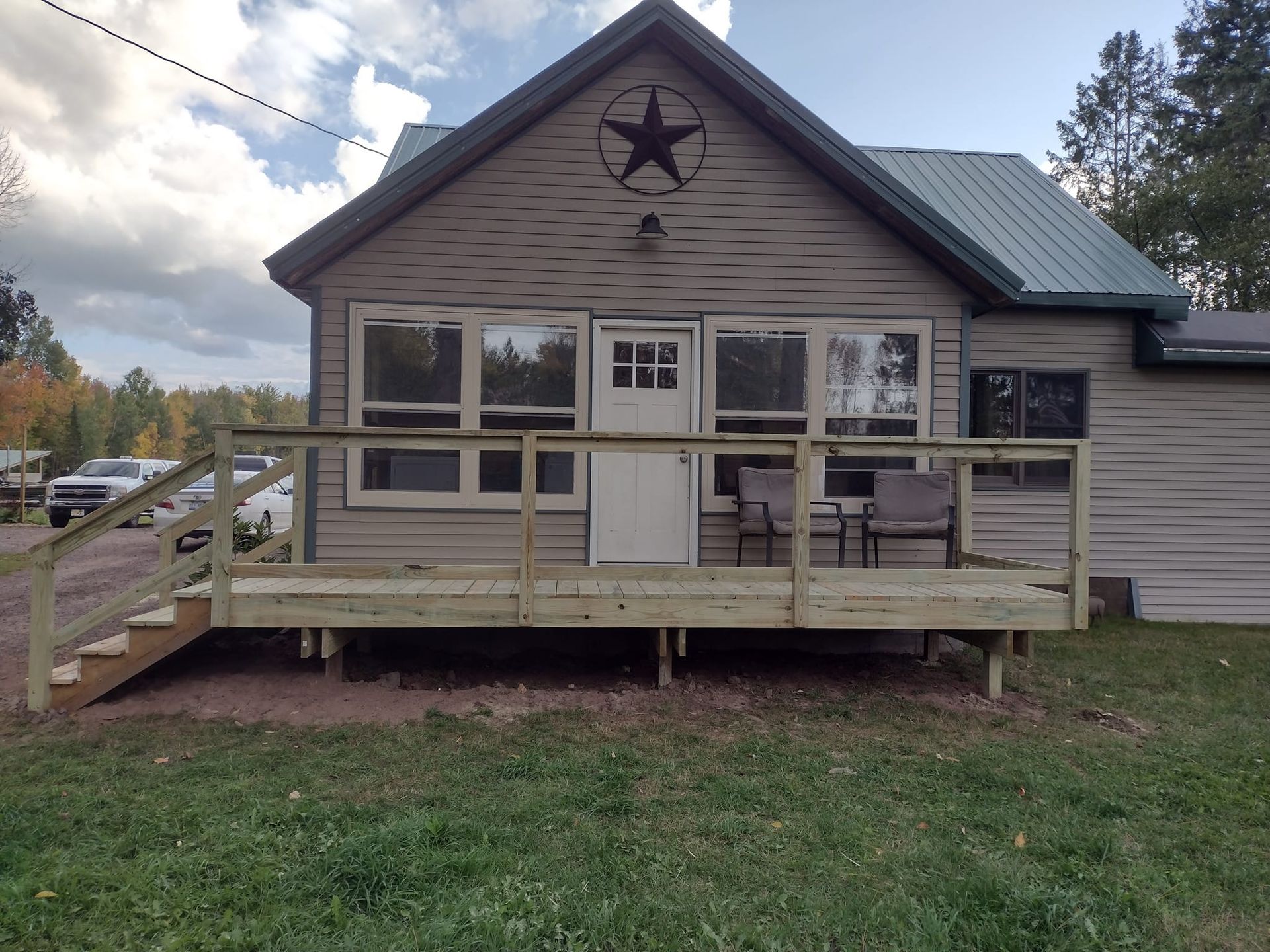 Cabin with a wooden deck, a star decoration, and several windows. Parked vehicles visible on the left.