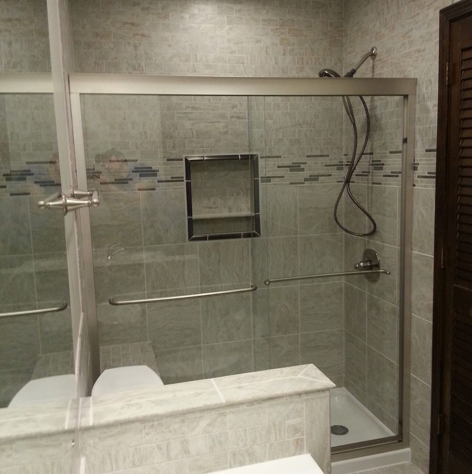 Bathroom with gray tile, glass shower door, built-in shelf, and grab bars.
