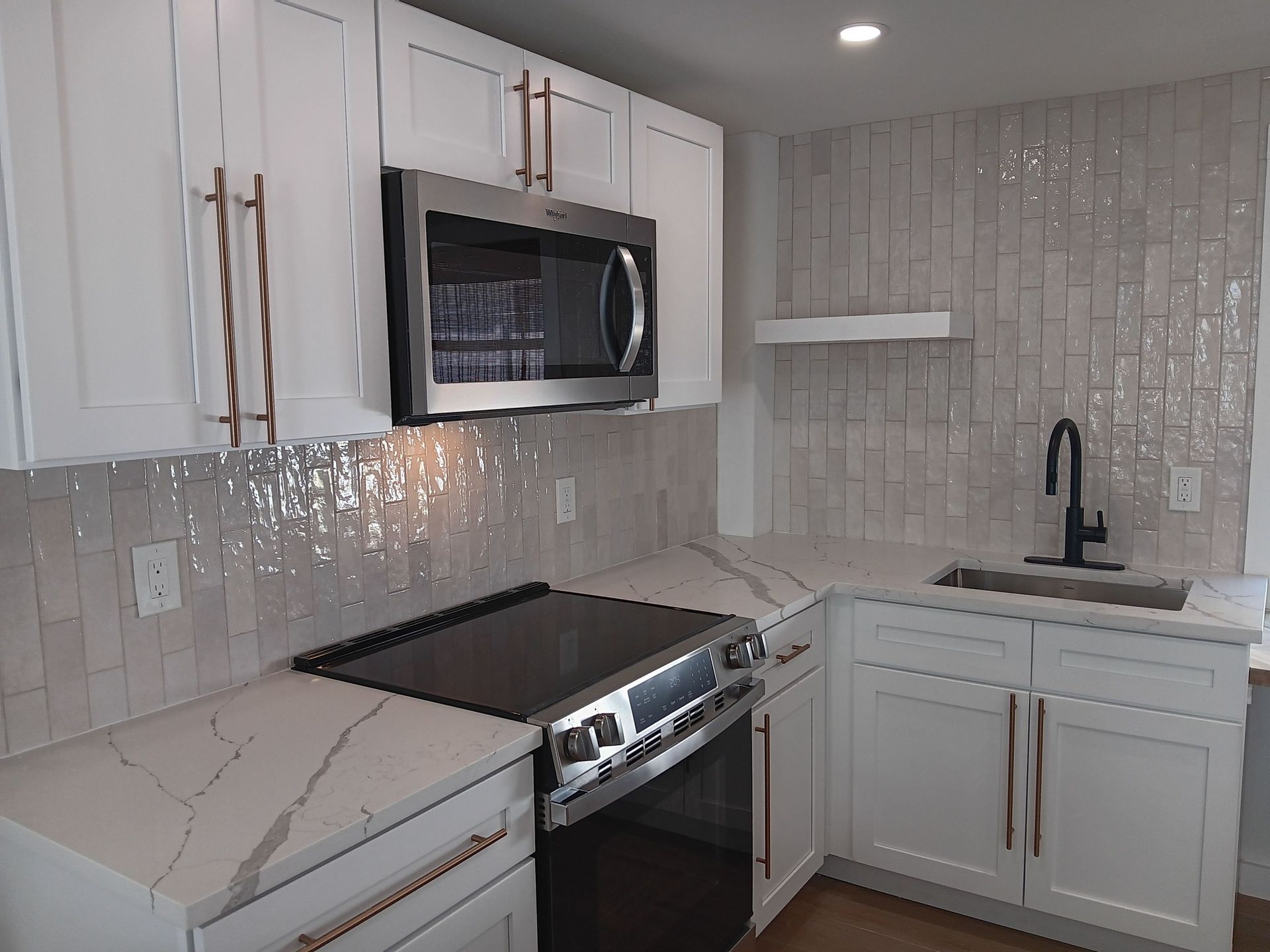 White kitchen with stainless steel appliances, marble countertops, and textured tile backsplash.