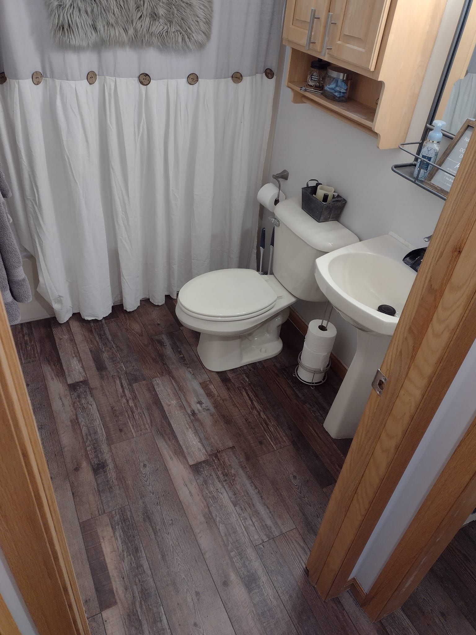 Small bathroom with white fixtures, wooden floors, and shower curtain.