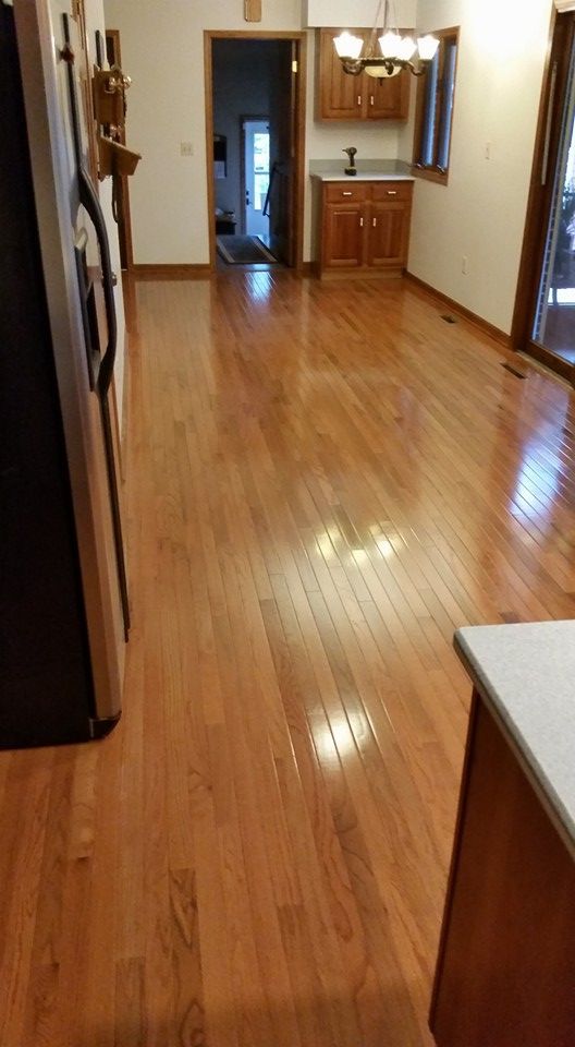 Hardwood floor in a kitchen area; shiny, light brown boards, with cabinets and fridge visible.