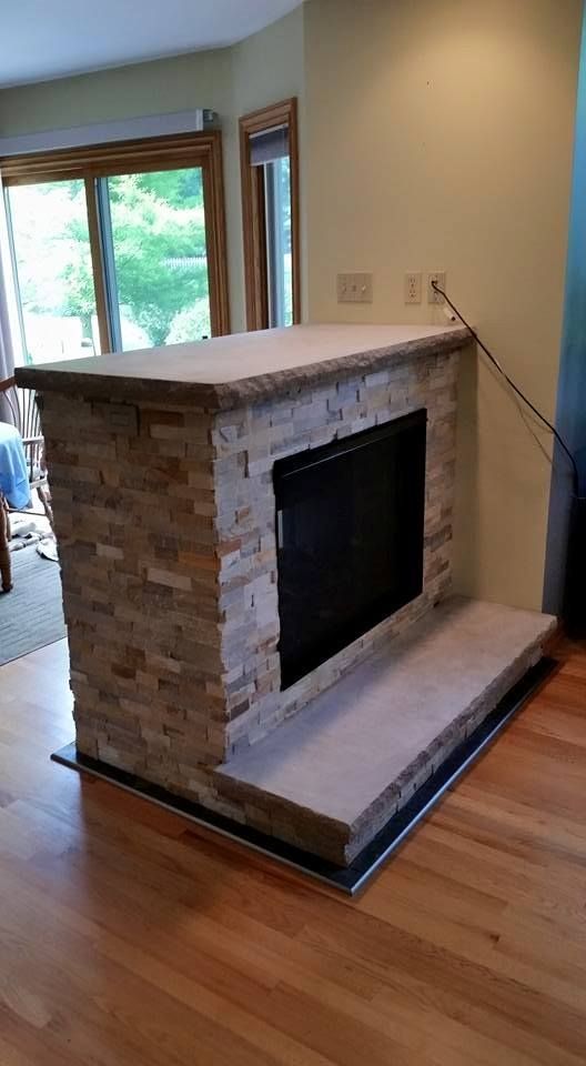 Fireplace with stone veneer, light countertop and hearth, wooden floor, beige walls.