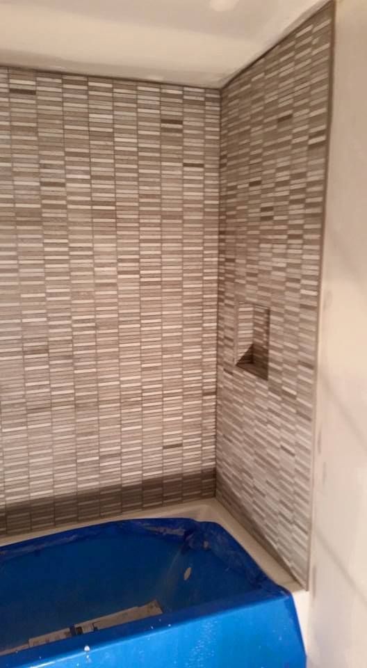 Bathroom corner with gray mosaic tile walls, a blue tub, and a built-in shelf.