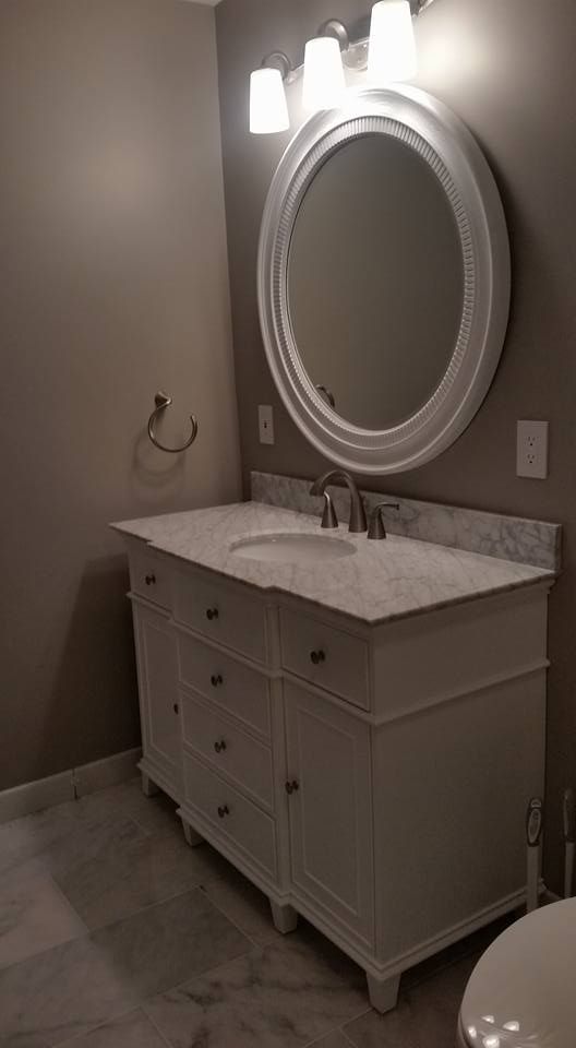 White bathroom vanity with oval mirror and light fixture.