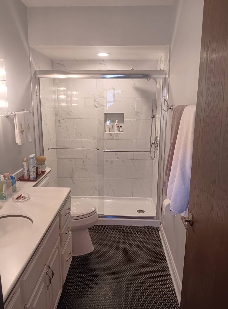 Bathroom with white marble shower, toilet, vanity, and black tiled floor. Towels hang on a rack.