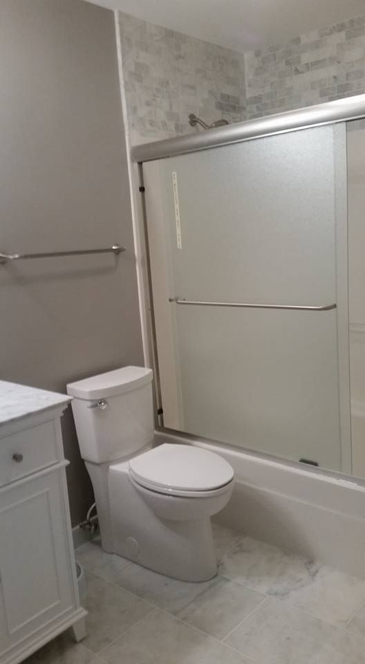 Bathroom with a white toilet, vanity, and shower. Gray walls, light-colored floor, and sliding glass shower door.