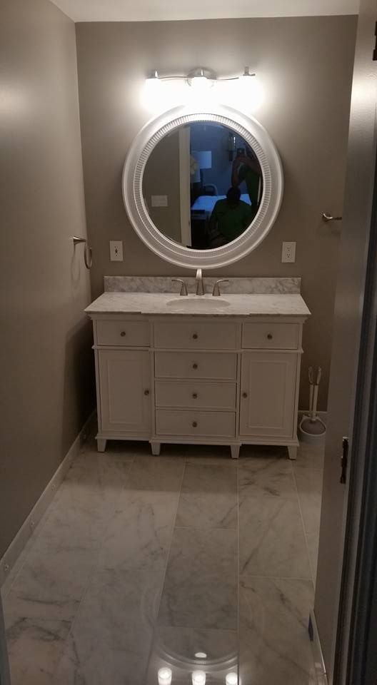 Bathroom with white vanity, marble countertop, round mirror, and tile floor.