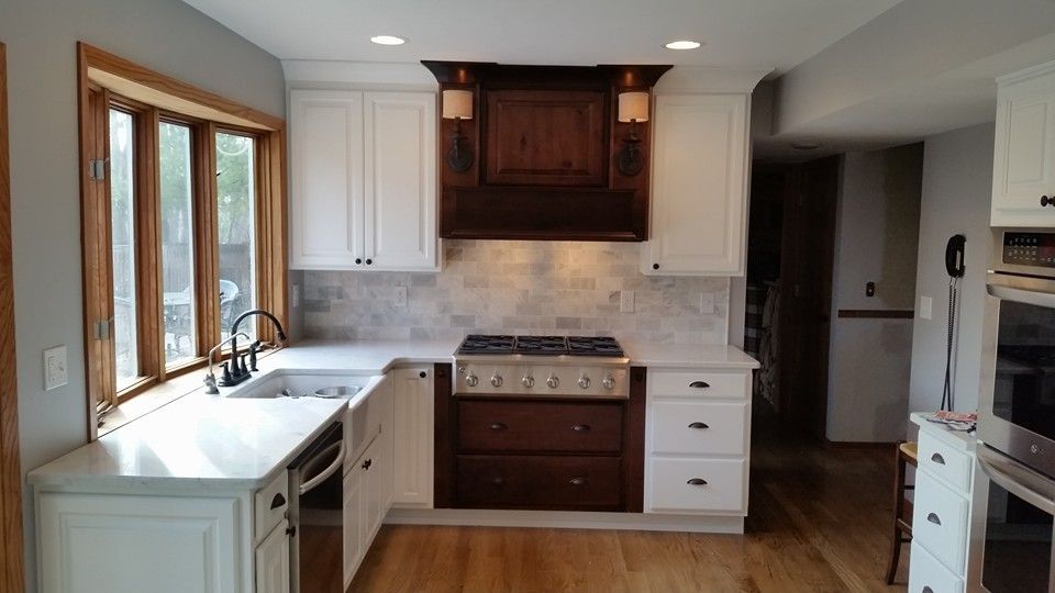 Kitchen remodel with white cabinets, dark wood range hood, and light-colored countertops.