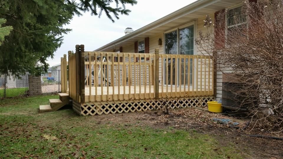 Wooden deck with lattice skirting, attached to a house with a sliding glass door and steps leading down to a grassy yard.