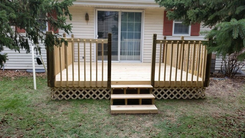 Wooden deck with lattice and railing, leading to a sliding glass door, three steps down to the grass.