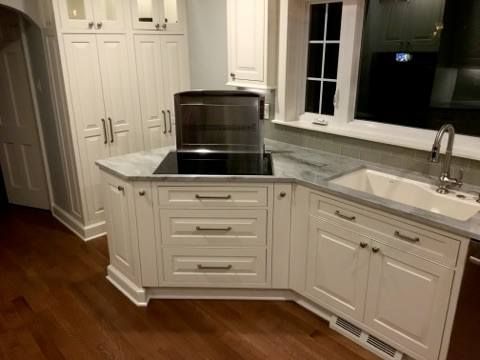 Cream-colored kitchen cabinets with a stovetop island, sink, and dark wood floors.
