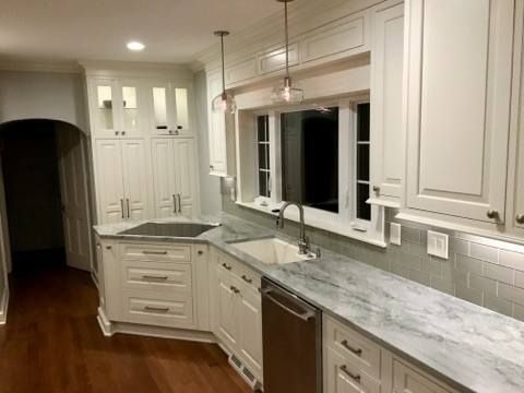 White kitchen with marble countertops, stainless steel appliances, and overhead lighting.