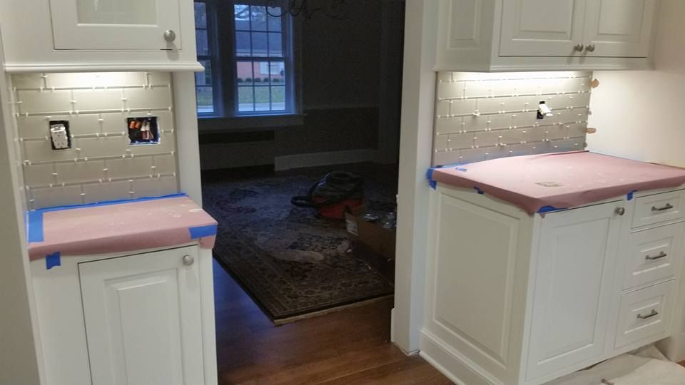 Two white cabinets with tiled backsplashes and lights, set in a doorway. Pink paper covers the counters.