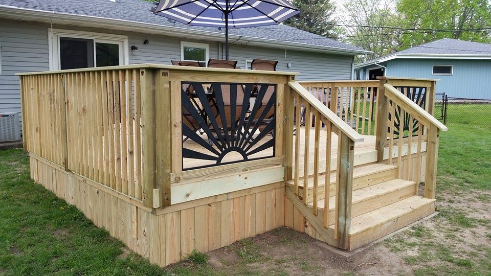 Wooden deck with steps, decorative panel, and umbrella.  Exterior view in a grassy yard.