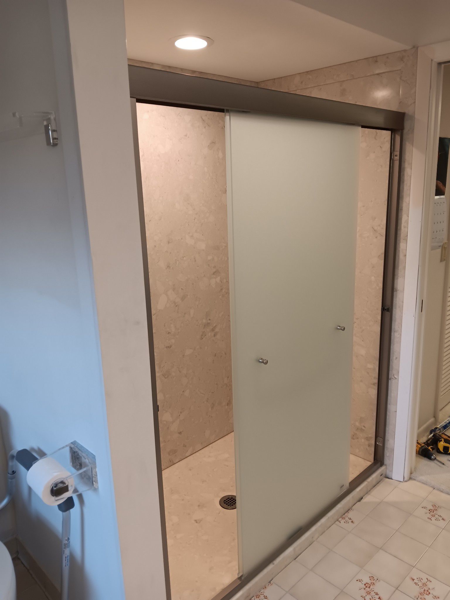 Shower stall with frosted glass sliding door, light tan stone tile walls, white trim.