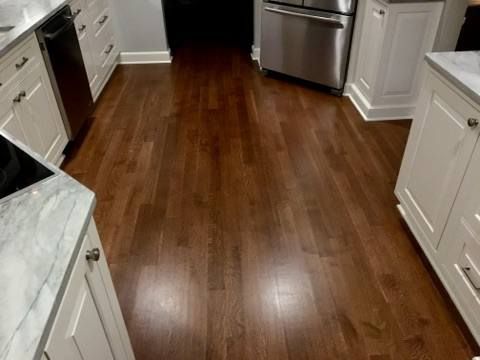 Hardwood flooring in a kitchen with white cabinets and stainless steel appliances.