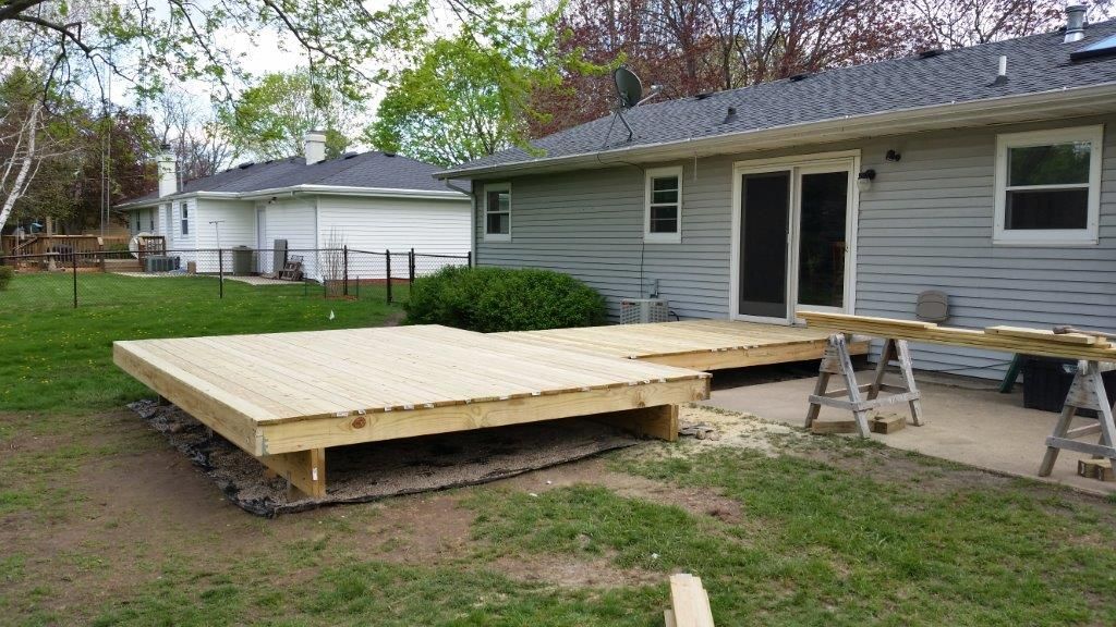 Wooden deck under construction in a grassy backyard, adjacent to a house with a sliding glass door.