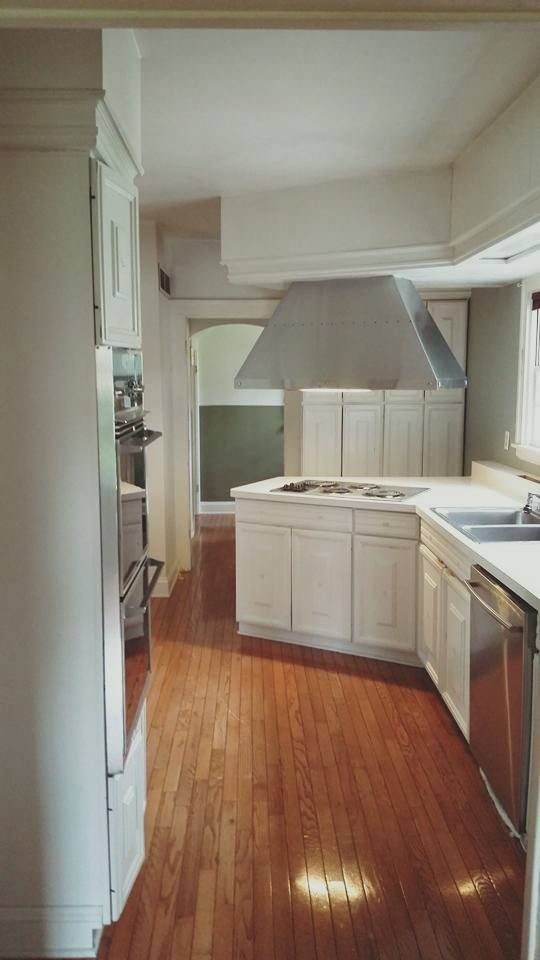 White kitchen with stainless steel appliances and hood vent, light wood floors, and open doorway.